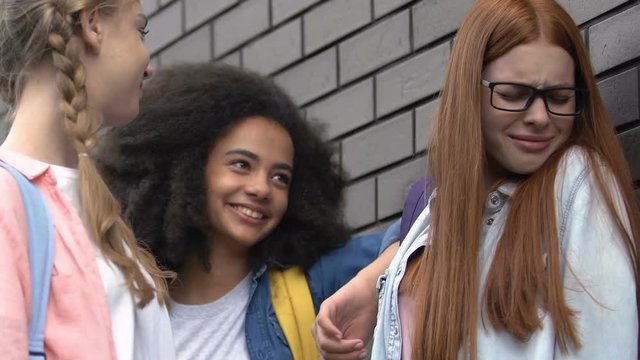 Student girls bullying female classmate, pushing to wall, mocking appearance