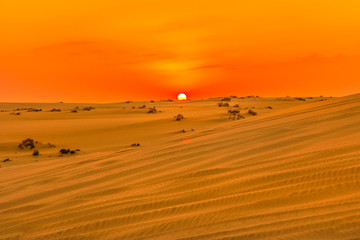 Fototapeta na wymiar Red and orange colors of sunset sky over sand dunes at Inland Sea. Desert landscape near Qatar and Saudi Arabia. Khor Al Udeid, Persian Gulf, Middle East. Discovery and adventure travel concept.