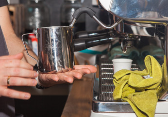 Fototapeta na wymiar Coffee shop in Los Angeles 19. June. 2019. Close-up of hands of barista making goof in cafe. Hand is holding an iron mug by the coffee machine.