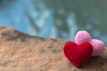 Red and pink hearts on stone with beautiful blurred background of waterfall