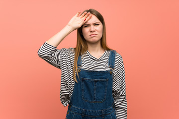 Young woman with overalls over pink wall with tired and sick expression