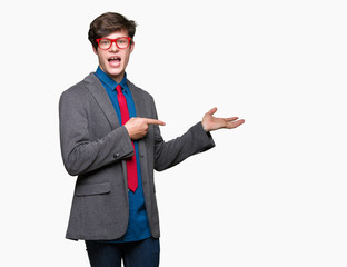 Young handsome business man wearing red glasses over isolated background amazed and smiling to the camera while presenting with hand and pointing with finger.