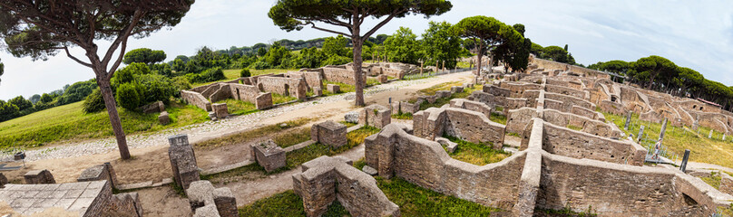 Fototapeta na wymiar Panoramic view - 180 degree in the excavation ruins at Ostia Antica - from the Decumanus Maximus to the gym of Neptune thermal baths with the view of the republican warehouses