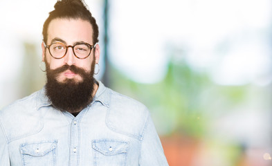 Young hipster man with long hair and beard wearing glasses puffing cheeks with funny face. Mouth...