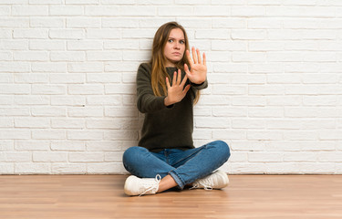 Fototapeta na wymiar Young woman sitting on the floor nervous stretching hands to the front