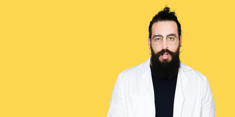 Doctor therapist man with long hair and bear wearing white coat afraid and shocked with surprise expression, fear and excited face.