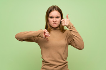 Young woman with turtleneck sweater making good-bad sign. Undecided between yes or not