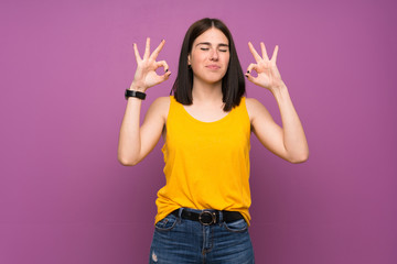 Young woman over isolated purple wall in zen pose