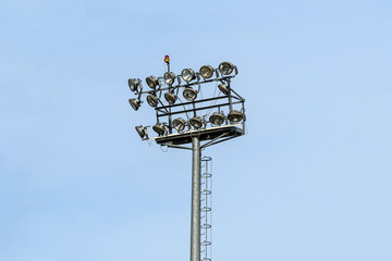 Two lines of stadium light spots or reflectors on a tall tower with clear blue sky in the background