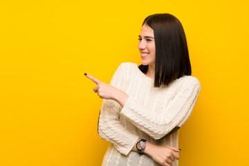 Young woman over isolated yellow wall pointing to the side to present a product