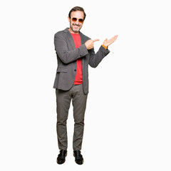 Middle age handsome business man wearing sunglasses amazed and smiling to the camera while presenting with hand and pointing with finger.