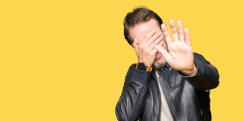 Middle age handsome man wearing black leather jacket covering eyes with hands and doing stop gesture with sad and fear expression. Embarrassed and negative concept.