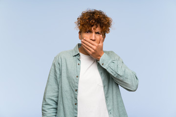 Young african american man over isolated blue wall covering mouth with hands
