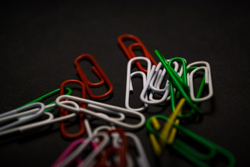 A set of multi-colored office paper clips of plastic are scattered on black monophonic background. 