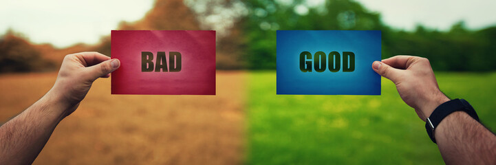 Man hands holding two colored paper sheets with opposite text good and bad over different nature...