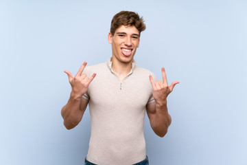 Handsome young man over isolated blue wall making rock gesture