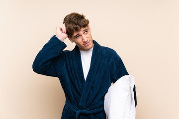 Handsome young man in pajamas over isolated wall having doubts and with confuse face expression