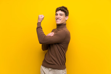 Handsome young man over isolated yellow background doing strong gesture