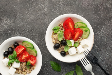 Healthy balanced appetizing salad bowl with quinoa, cucumber, tomatoes, feta cheese, olives, basil leaves on a gray background in a white plate