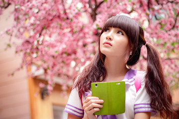 Beautiful Asian model in Japanese student uniform with cherry blossom flower in background