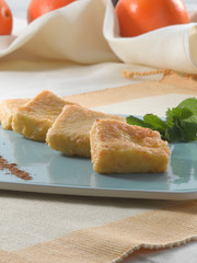 Leche frita con canela y azúcar  sobre plato azul,  vista cenital. Fried milk with cinnamon and sugar on a blue plate, overhead view.