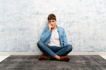 Handsome young man sitting on the floor nervous and scared