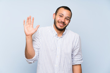 Fototapeta premium Colombian man over isolated blue wall saluting with hand with happy expression