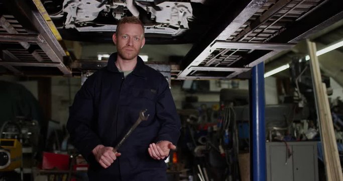 4K Serious mechanic posing with wrench underneath vehicle ramp. Slow motion.