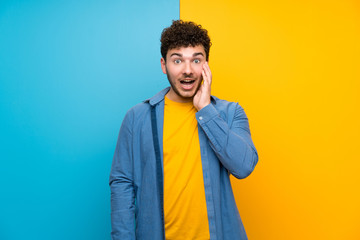 Man with curly hair over colorful wall with surprise and shocked facial expression
