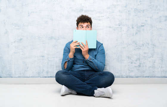 Young man sitting on the floor holding and reading a book