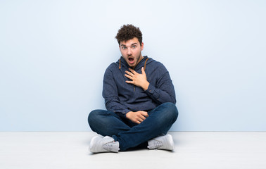 Young man sitting on the floor surprised and shocked while looking right