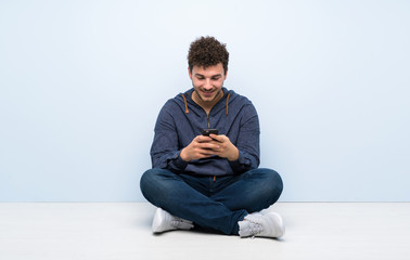 Young man sitting on the floor sending a message with the mobile