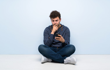 Young man sitting on the floor thinking and sending a message