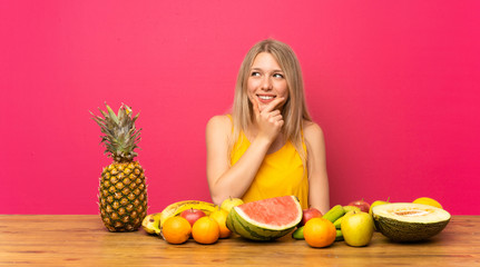 Young blonde woman with lots of fruits thinking an idea