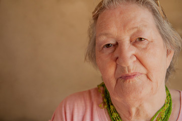 Portrait of elderly woman in pink T-shirt with decorations and glasses. Pensioner supports health and looks great with beautician bag