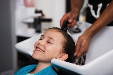 Hairdresser washing hair of cute girl in hair salon. 