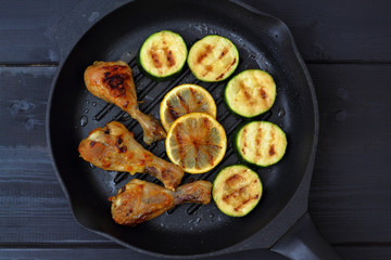 grilled chicken, tomato sauce and zucchini on a griddle, black background