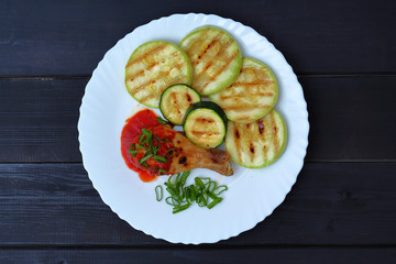 grilled chicken, tomato sauce and zucchini on a plate, black background