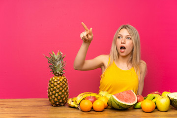 Obraz premium Young blonde woman with lots of fruits pointing away