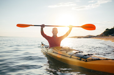 Smiling senior man in kayak holds paddles high