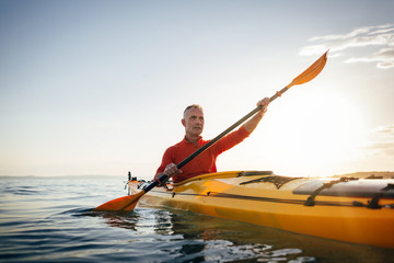 Senior man paddling kayak on the sunset sea. Acitve vacation, kayaking, paddling, canoeing - obrazy, fototapety, plakaty