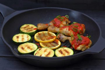 grilled chicken, tomato sauce and zucchini on a griddle, black background