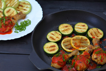 grilled chicken, tomato sauce and zucchini on a plate, black background