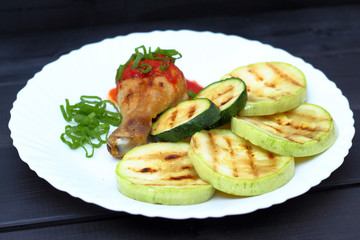 grilled chicken, tomato sauce and zucchini on a plate, black background