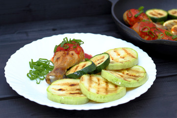 grilled chicken, tomato sauce and zucchini on a plate, black background