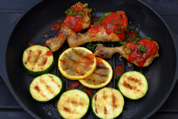grilled chicken, tomato sauce and zucchini on a griddle, black background