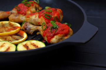 grilled chicken, tomato sauce and zucchini on a griddle, black background