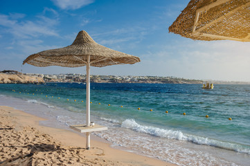 Thatched beach umbrellas and loungers on a beach at an idyllic tropical resort for a summer vacation