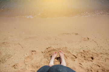 top view of woman's legs and hat relaxing on the beach