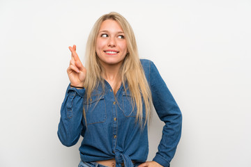 Young blonde woman over isolated white wall with fingers crossing and wishing the best